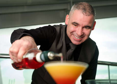 A member of bar staff pouring a red liquid into an orange cocktail.