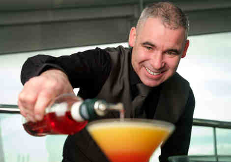 A member of bar staff pouring a red liquid into an orange cocktail.