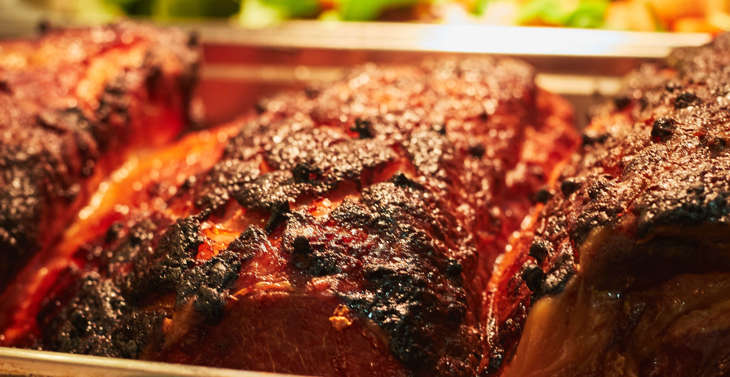 A metal tray containing cooked meats in front of another containing cooked vegetables.