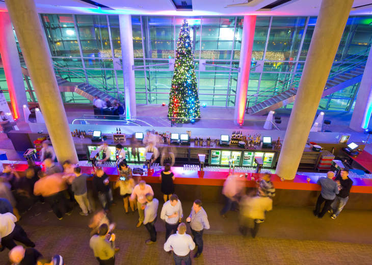 A birds eye view of attendees enjoying a Christmas party on a balcony at the Aviva Stadium with a large decorated Christmas tree in the background.