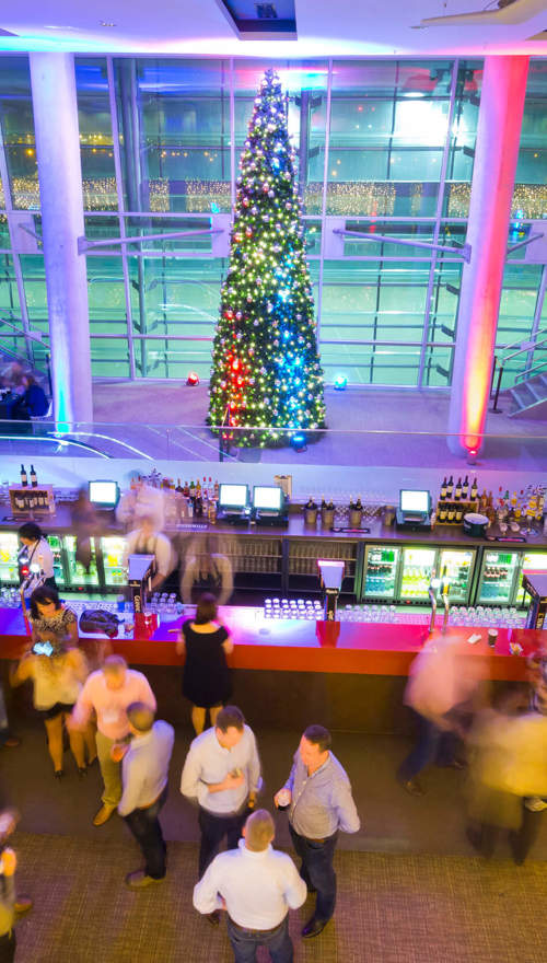 A birds eye view of attendees enjoying a Christmas party on a balcony at the Aviva Stadium with a large decorated Christmas tree in the background.