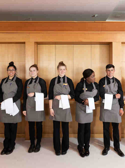 7 members of staffing standing in a line looking at the camera whilst holding napkins.
