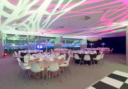 A group of tables set and decorated ready for a dining event with purple lighting.