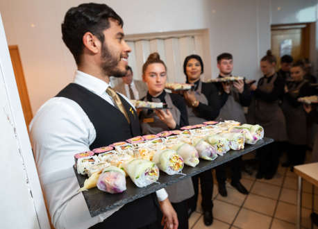 A group of waiting staff carrying sushi on black boards.