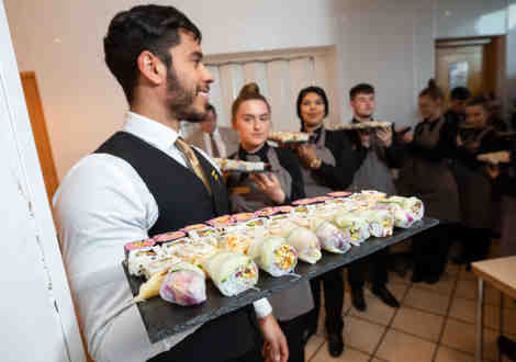 A group of waiting staff carrying sushi on black boards.