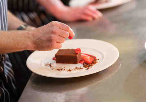 A hand preparing a chocolate cake with sliced strawberries on a white plate.