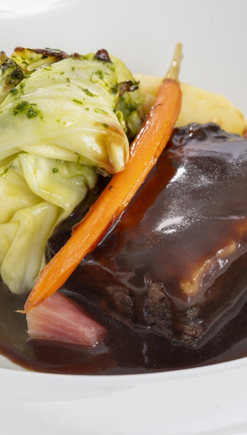 A dish containing cooked meat in gravy with a carrot, cabbage and mashed potato.
