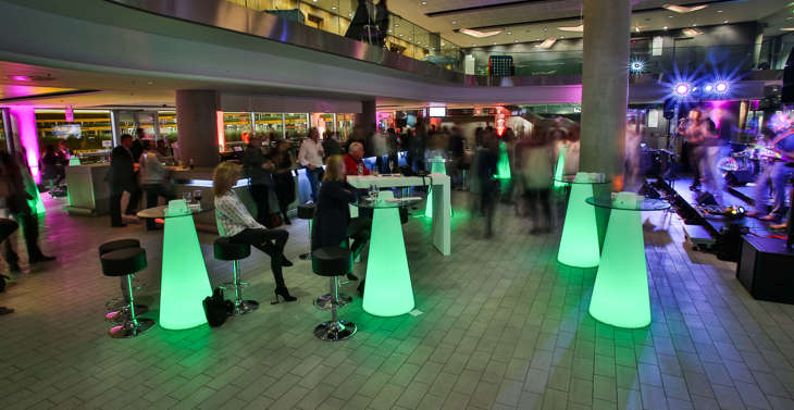 An event at the Aviva Stadium with attendees ordering drinks at a bar and sat at green tables watching a live band.
