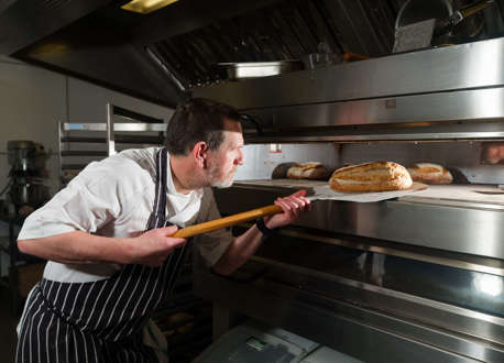 A chef removing a loaf of bread from an oven. 
