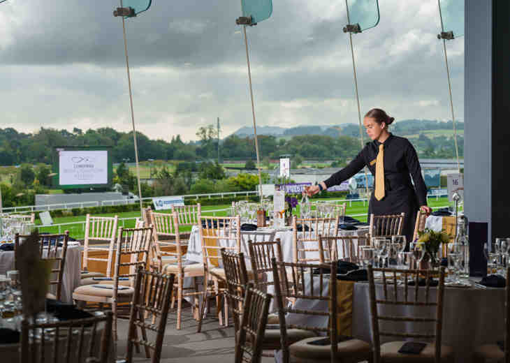 A young woman arranging and setting table decorations before an event at a racecourse.