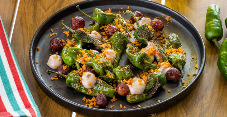 Cooked peppers and vegetables and sauce served on a black plate on a wooden surface.