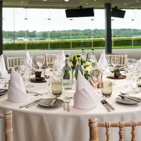A round table set for dinner with a view of the racecourse through a large window.