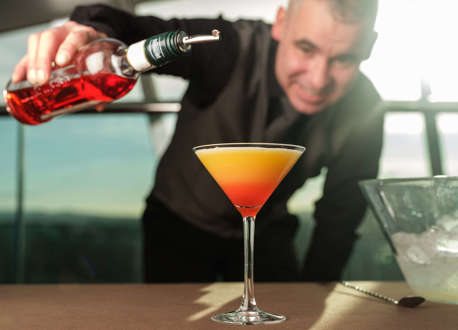 A waiter pouring a bottle to create an orange cocktail.