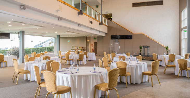 A hall filled with round tables and chairs with an upstairs concourse area above.