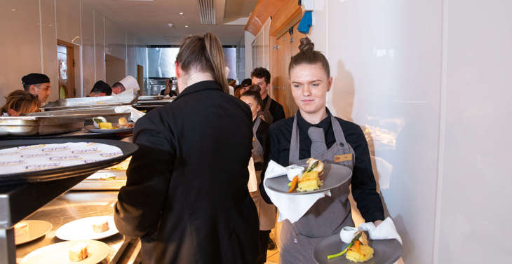 A waitress carrying plates of food out of a kitchen.