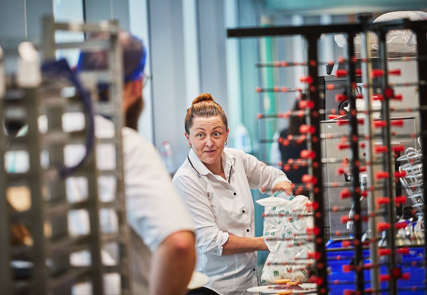 A female chef talking to a male chef with his back to the camera in a kitchen.