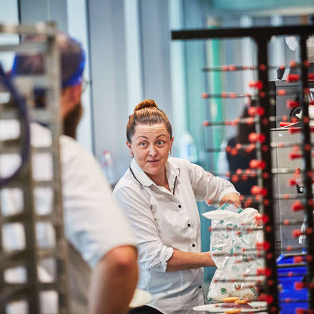 A female chef talking to a male chef with his back to the camera in a kitchen.