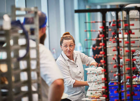 A female chef talking to a male chef with his back to the camera in a kitchen.