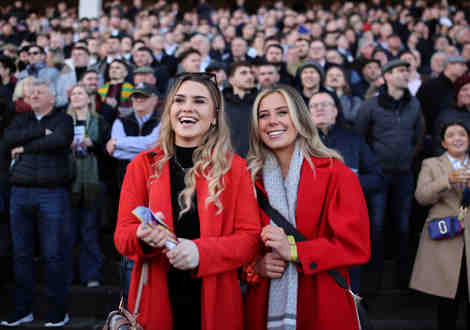 Two women wearing red coats standing in the crowd at a racecourse.