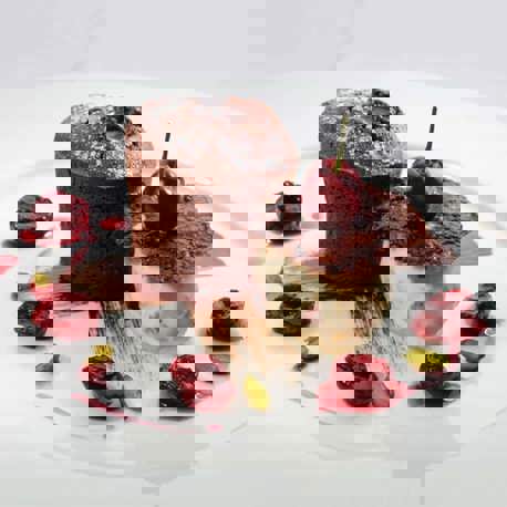 A chocolate cake and a dessert topped with a cherry on a white polate served with cherries.