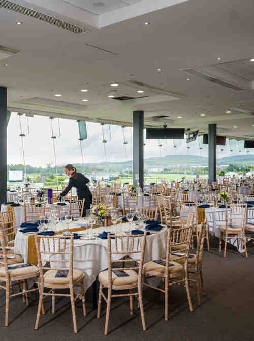 Two members of staff setting tables in large hall at Leopardstown Racecourse.