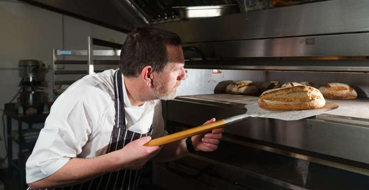 A chef removing a loaf of bread from an oven.
