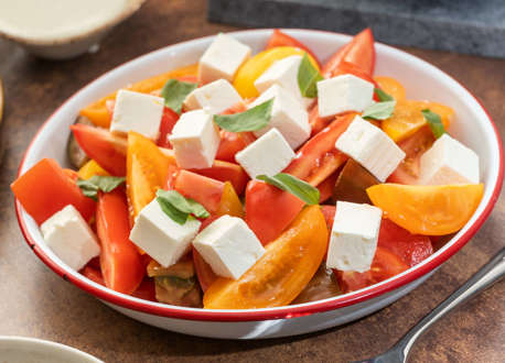 A bowl of sliced tomatoes and cheese next to a spoon and more bowls of food.
