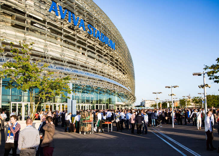 A crowd made up of different groups of people drinking and talking outside an event at the Aviva Stadium.