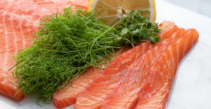 Slices of salmon served on a marble board served with lemon, salad and herbs.
