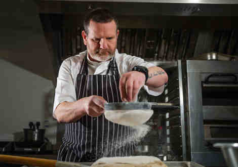 A chef topping dough with flour through a sieve. 