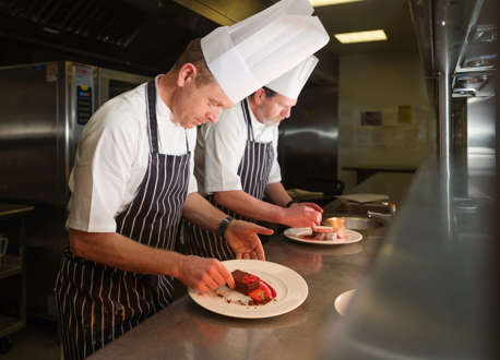 Two chefs standing over plated desserts on a kitchen counter.
