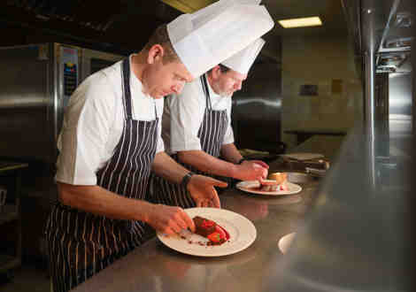 Two chefs standing over plated desserts on a kitchen counter.