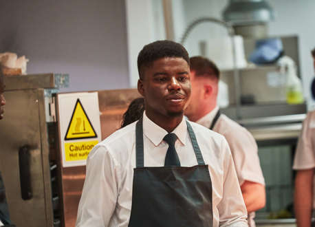 A waiter carrying a wooden tray of food through a kitchen.