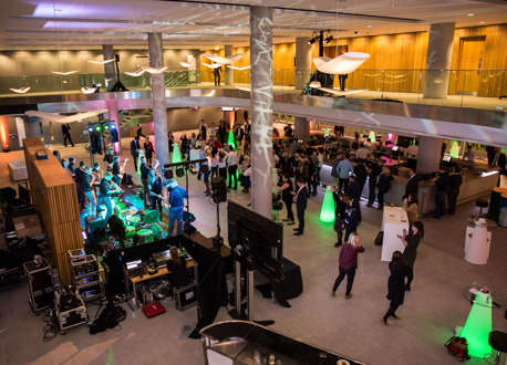 An aerial view of a band playing in a foyer to a crowd of people with people standing at a bar in the background.
