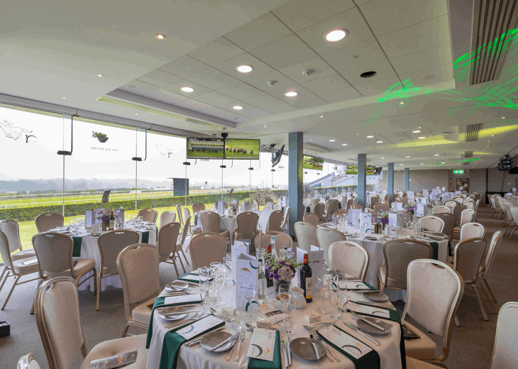 The Lower Pavilion overlooking the racecourse at Leopardstown set up for a dinner with round tables.