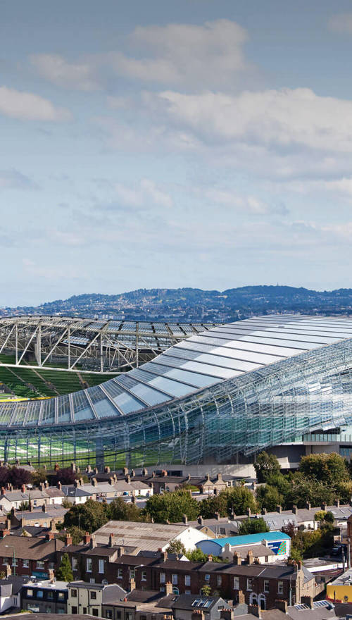 An aerial view of the Aviva Stadium, the surrounding houses, a passing train and the waterfront in the background.