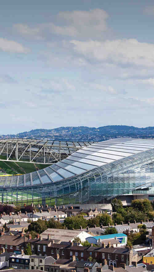 An aerial view of the Aviva Stadium, the surrounding houses, a passing train and the waterfront in the background.